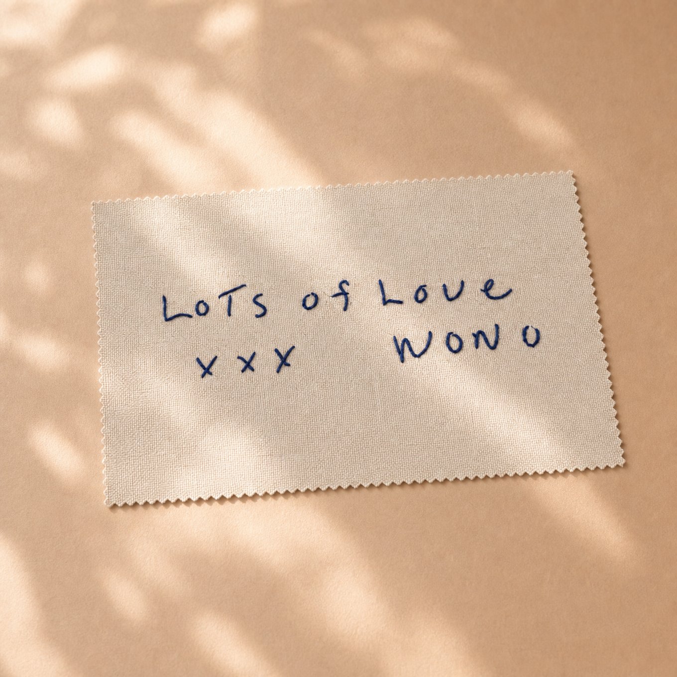 Unframed embroidered fabric reading "lots of love xxx Wono"